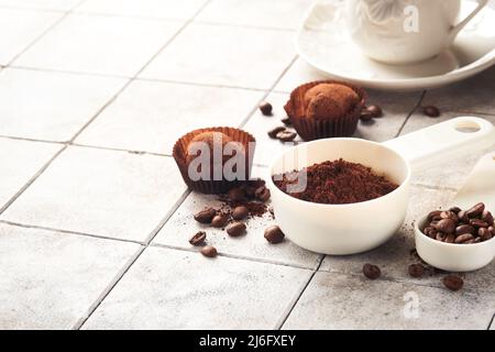 Sfondo del caffè. Cucchiai di misurazione con caffè macinato, fagioli, tazza e tartufi di cioccolato dolce su piastrelle di fondo vecchio tavolo incrinato. Sfondo alimentare. Foto Stock