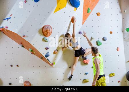 Scalatori di roccia in palestra di arrampicata. Giovane donna arrampicata problema bouldering (percorso), l'uomo che le dà le istruzioni. Foto Stock