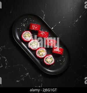 Tradizionale e delizioso sushi roll fresco su sfondo nero. Sushi roll con riso, nori, formaggio cremoso, caviale tobiko, avocado. Menu di sushi. Giapponese Foto Stock