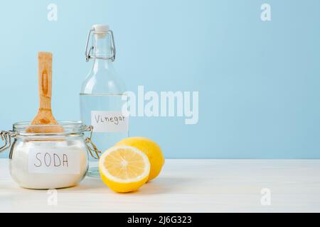 Aprire il vaso di bicarbonato con un cucchiaio di legno sulla parte superiore, aceto, limone tagliato, su sfondo blu. Il concetto di rimozione organica macchie sui vestiti. Foto Stock