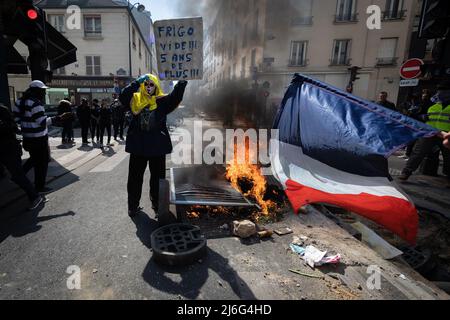 Un manifestante giallo con una bandiera francese cammina accanto a mobili di strada brucianti che è stato messo a fuoco per impedire alla polizia di andare avanti. Migliaia di persone si sono svolte per i raduni del giorno di maggio. I manifestanti hanno marciato attraverso la città chiedendo il progresso sociale in una società ansiosa per il futuro del pianeta e di un mondo in pace. Storicamente il 1st maggio segna la Giornata Internazionale del lavoro che commemora i lavoratori e la classe operaia. Foto Stock