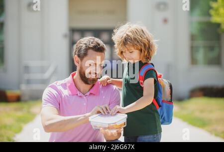 Pranzo scolastico per bambini. Il Padre sostiene e motiva il figlio. Scolaro e genitore in camicia che tiene il pranzo al sacco. Foto Stock