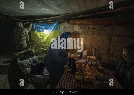 Lyubov Ivanovna Vlasenko, 70, centro, e suo marito Gennady Ivanovich Sergeev, 74, giusto, si preparano a mangiare mentre Vitaly Ignatov, 52, appende la bandiera Ucraina nel seminterrato-trasformato bunker solo pochi istanti dopo che l'artiglieria russa sbarcò a circa 800 metri di distanza nel distretto di Pyatikhatki, di Kharkiv, Ucraina, 1 maggio 2022. Il presidente della Camera Nancy Pelosi ha guidato la prima delegazione ufficiale dei legislatori in Ucraina ed è diventato il funzionario più anziano degli Stati Uniti per incontrare il presidente Volodymyr Zelenskysince la Russia ha invaso il febbraio 24, secondo una dichiarazione rilasciata Domenica. Credit: UPI/Alamy Live N Foto Stock