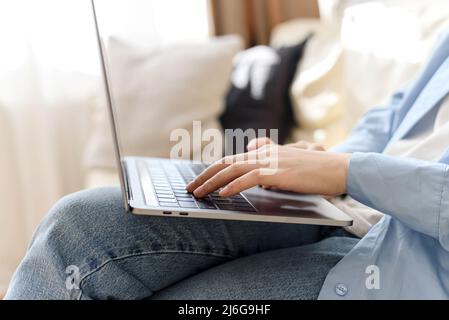 Primo piano delle mani della donna sulla tastiera del laptop mentre si siede sul divano a casa. Lavoro freelance da casa, navigare in Internet. Foto Stock