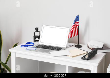 Posto di lavoro con un moderno computer portatile, lettere e bandiera USA vicino alla parete della luce Foto Stock