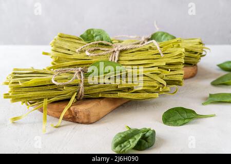 Fasci di fettuccine di pasta cruda con spinaci su tagliere in legno e fondo in calcestruzzo Foto Stock