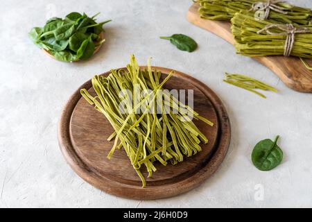 Fettuccine di pasta cruda con spinaci su tagliere in legno e fondo in calcestruzzo Foto Stock