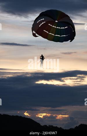 Due persone (un allenatore e un tirocinante, visto solo come una silhouette) sotto la cupola del paracadute paracadutista paracadutista, contro il cielo di tarda sera Foto Stock