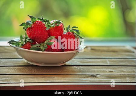 Ciotola bianca con fragole su tavola di legno su sfondo naturale Foto Stock