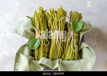 Fasci di fettuccine di pasta cruda con spinaci messi in scatola con tovagliolo verde e fondo in calcestruzzo Foto Stock
