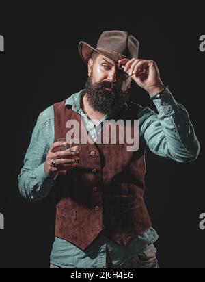 Uomo barman con barba tiene il brandy di vetro. Uomo fiducioso in abito nero con bicchiere di whisky in loft. Bevanda alcolica. Foto Stock