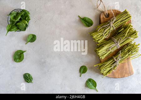 Fasci di fettuccine di pasta cruda con spinaci su tagliere in legno e fondo in calcestruzzo Foto Stock