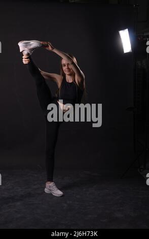 Una ragazza di spago nera in su sfondo calci Un karate arti isolate marziali, per la seduta blu per il calcio per cintura di potenza, salute uniforme. Orizzontale Foto Stock