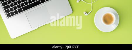 Banner di tastiera metallica per computer portatile, auricolari bianchi e tazza da caffè su sfondo verde chiaro Foto Stock