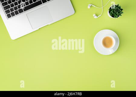 Orizzontale di tastiera metallica per computer portatile, auricolari bianchi e tazza da caffè su sfondo verde chiaro Foto Stock