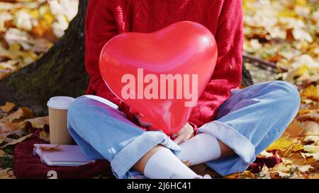 Primo piano di un pallone a forma di cuore rosso tenuto da una persona in un parco autunnale. Concetto di amore. Foto di alta qualità Foto Stock