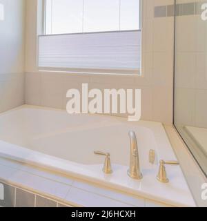 Vasca da bagno quadrata in un angolo contro la finestra con persiane Foto Stock