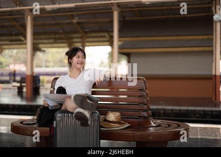 Felice giovane asiatica viaggiatore o zaino in spalla utilizzando mappa scegliere dove viaggiare con i bagagli alla stazione ferroviaria, vacanza estiva concetto di viaggio Foto Stock