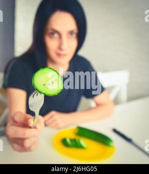 Giovane donna attraente mostra cetriolo su forchetta. Dieta vegetariana, perdita di peso e snellente concetto copypaste sfondo verticale Foto Stock
