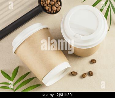 Caffè da gustare. Due tazze di cartone ecologico monouso con chicchi di caffè naturali sulla sabbia con foglie di palma. Caffè da asporto. Vacanza wit Foto Stock