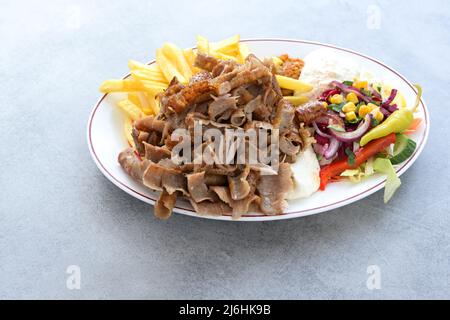 Fette sottili di kebab doner con patatine fritte, insalata e yogurt salsa di immersione su un piatto e un tavolo grigio, spazio copia, fuoco selezionato, profondità stretta di Foto Stock