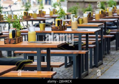 Panchine di legno e tavoli in un ristorante di strada nel centro della città, gastronomia urbana all'aperto, fuoco selezionato, profondità di campo stretta Foto Stock