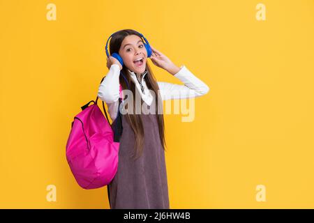 il bambino è rimasto sorpreso dalle cuffie con lo zaino della scuola su sfondo giallo Foto Stock