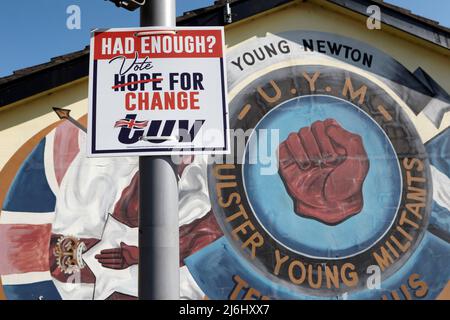 TUV (Traditional Unionist Voice) poster elettorale accanto ai murales paramilitari Loyalist su 'Freedom Corner' Lower Newtownards Road, East Belfast, North Foto Stock