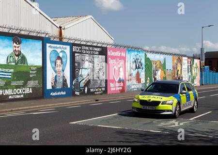 L'auto di pattuglia della polizia PSNI passa i murales repubblicani 'International Wall' sulla Lower Falls Road West Belfast, Irlanda del Nord, 20th aprile 2022. Foto Stock