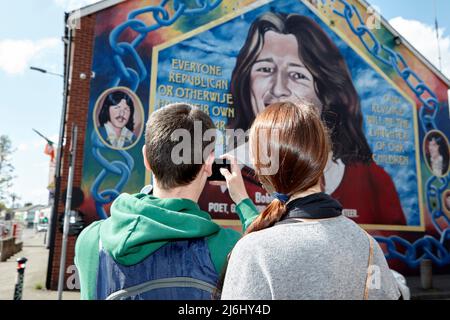 Coppia di turisti dalla Spagna scattare foto al murale di Bobby Sands sulla parete dell'ufficio del Sinn Fein, Lower Falls Road, West Belfast, Irlanda del Nord, Foto Stock