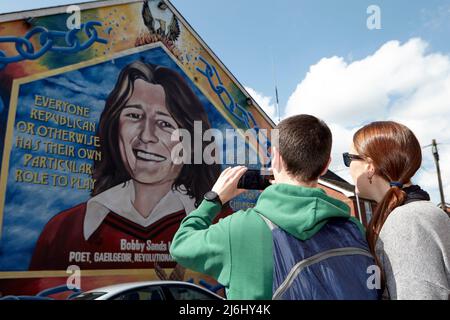 Coppia di turisti dalla Spagna scattare foto al murale di Bobby Sands sulla parete dell'ufficio del Sinn Fein, Lower Falls Road, West Belfast, Irlanda del Nord, Foto Stock