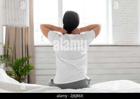 Uomo che soffre di dolore al collo a casa in camera da letto Foto Stock