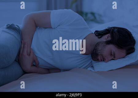 Uomo malato che soffre di crampi di stomaco di notte Foto Stock