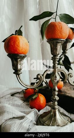 Ancora vita con porta candela in metallo d'epoca e mandarini su sfondo bianco di stoffa. Foto Stock