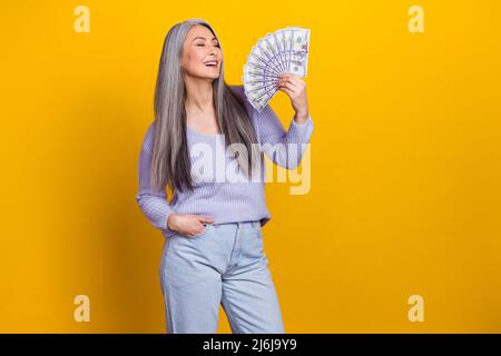 Foto di ragazza allegra mature mature milionario fresco usando i soldi come ventilatore sensazione di isolamento libero su sfondo giallo Foto Stock