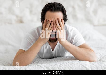 Primo piano dell'uomo bearded che steso nel letto, yawning Foto Stock