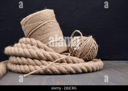 Corda di iuta e rocchetti di fili di tela o spago di iuta in primo piano su legno rustico su sfondo nero con spazio copia Foto Stock