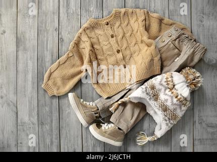 Cardigan lavorato a maglia, jeans e cappello piatto su sfondo di legno. Baby abiti autunnali. Set abbigliamento ragazzo.Vista dall'alto abbigliamento bambino.raccolta di Outlook vi Foto Stock