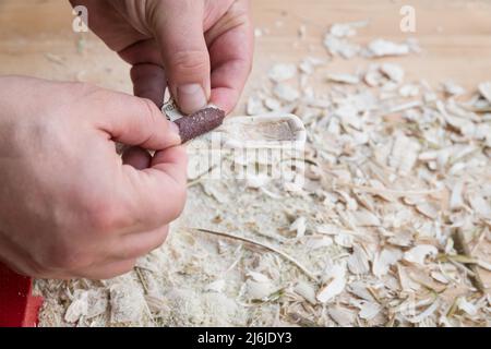 Cucchiaio di legno autointagliato bloccato in morsa lavorato con carta vetrata su un banco da lavoro con trucioli di legno, Germania Foto Stock