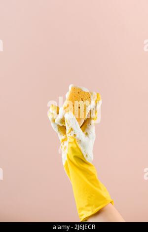 La persona in guanto di gomma tiene la spugna con le piastre di lavaggio di schiuma sul closeup beige Foto Stock