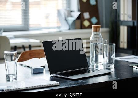 Primo piano di laptop aperto e bottiglia d'acqua sul tavolo da riunione in ufficio, spazio per fotocopie Foto Stock