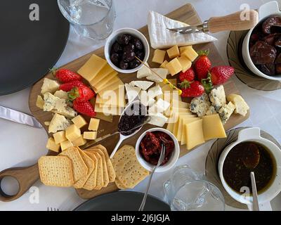 Piatto di formaggi con camembert, brie, dor blue, fragole, pomodori secchi, olive su un tavolo di legno, vista dall'alto. Foto Stock