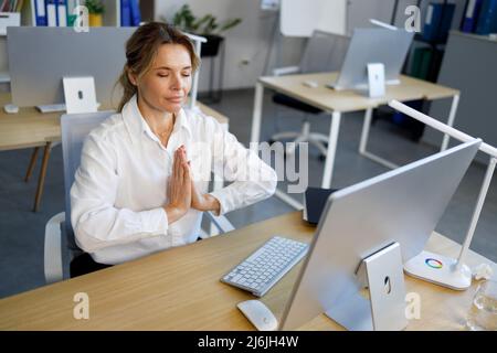 Donna d'ufficio concentrata meditating mentre si siede alla scrivania d'ufficio con gli occhi chiusi. . Ritratto di una donna calmo bianco colletto lavoratore Foto Stock
