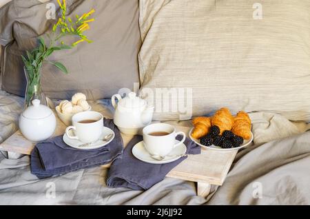 La prima colazione a letto : Teiera, due tazza di tè, croissant e meringa sul vassoio in legno Buona mattina scenario dello sfondo. Lo stile scandinavo. Foto Stock