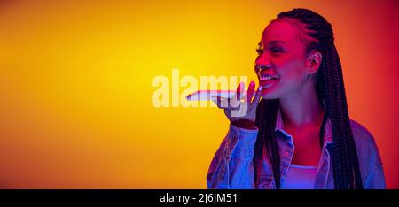 Ragazza bella giovane in camicia di cotone usando il telefono isolato su sfondo giallo rosso in luce al neon. Concetto di bellezza, arte, moda, gioventù ed emozioni Foto Stock