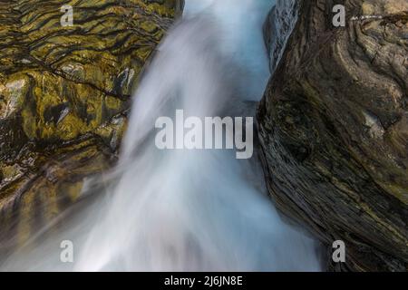 Tra le rocce cade un ruscello montano infestante di acqua limpida fotografata con la sfocatura del movimento. Foto Stock