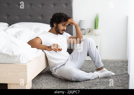 Ragazzo indù depresso che beve alcol, seduto al piano a letto Foto Stock
