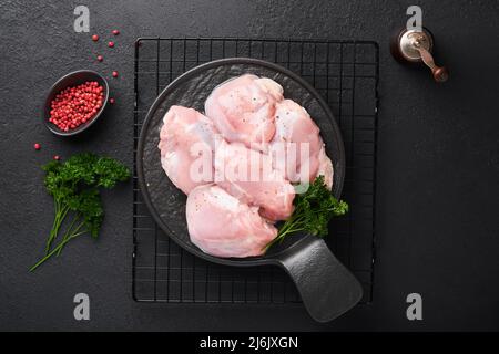 Filetto di coscia di pollo crudo senza pelle con erbe e spezie su sfondo nero. Carne di pollame di fattoria. Vista dall'alto con spazio di copia. Mock up. Foto Stock