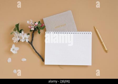 Scrivania da ufficio. Blocco note o pianificatore, penna e delicati fiori di mela. Vista dall'alto. Disposizione piatta. Spazio di lavoro per uffici domestici. Spazio copia, simulazione Foto Stock