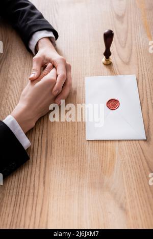 vista parziale dell'avvocato vicino a stampatore e busta sigillata con cera su scrivania in legno Foto Stock